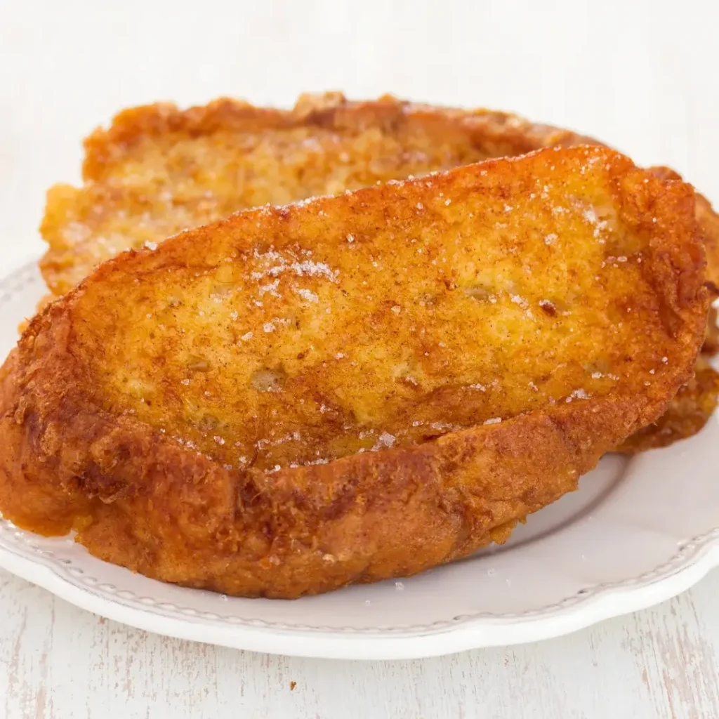 Fatias de pão douradas sobre prato branco com açúcar e canela