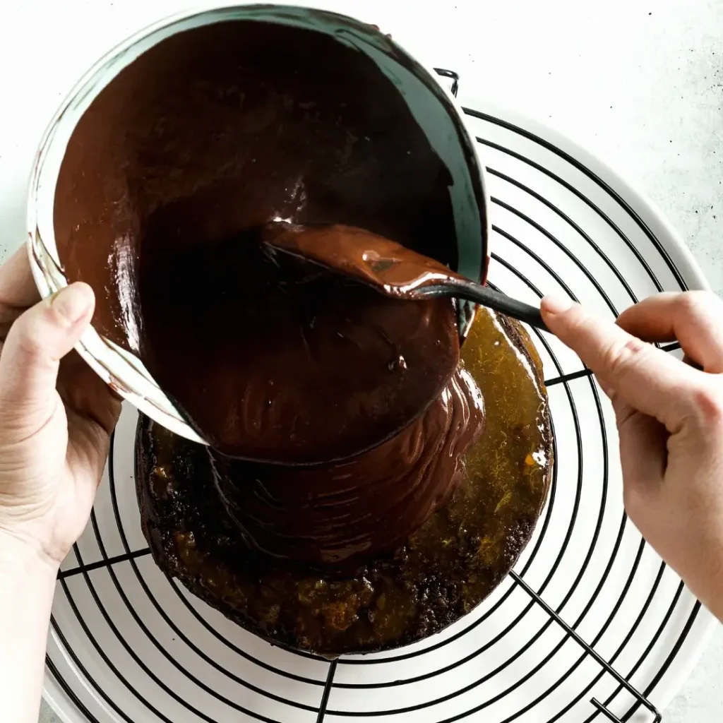 Mãos despejando ganache de chocolate meio amargo sobre o topo de um bolo