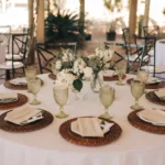 Mesa de jantar formal com pratos brancos, talheres e guardanapos de pano em formato de leque dentro das taças