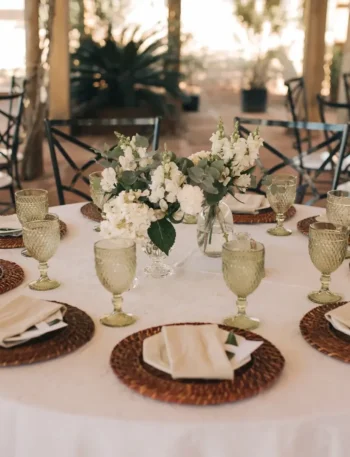 Mesa de jantar formal com pratos brancos, talheres e guardanapos de pano em formato de leque dentro das taças