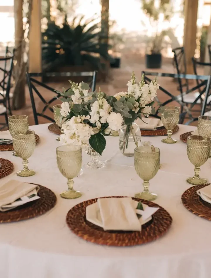 Mesa de jantar formal com pratos brancos, talheres e guardanapos de pano em formato de leque dentro das taças