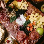 Tábua de madeira repleta de queijos, salames, frutas e nozes